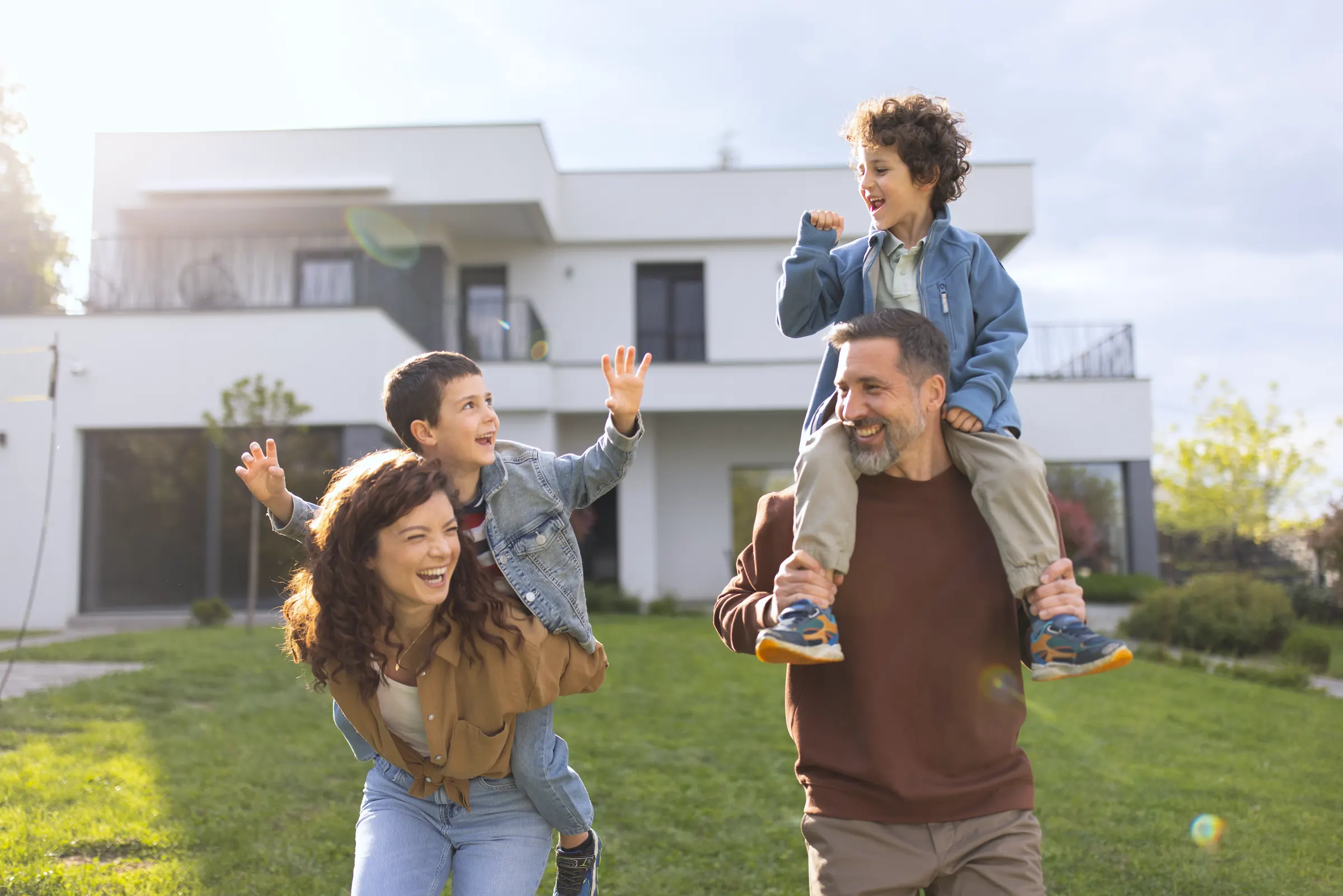 Familie mit zwei Söhnen tobt lachend im Garten vor ihrem modernen Haus