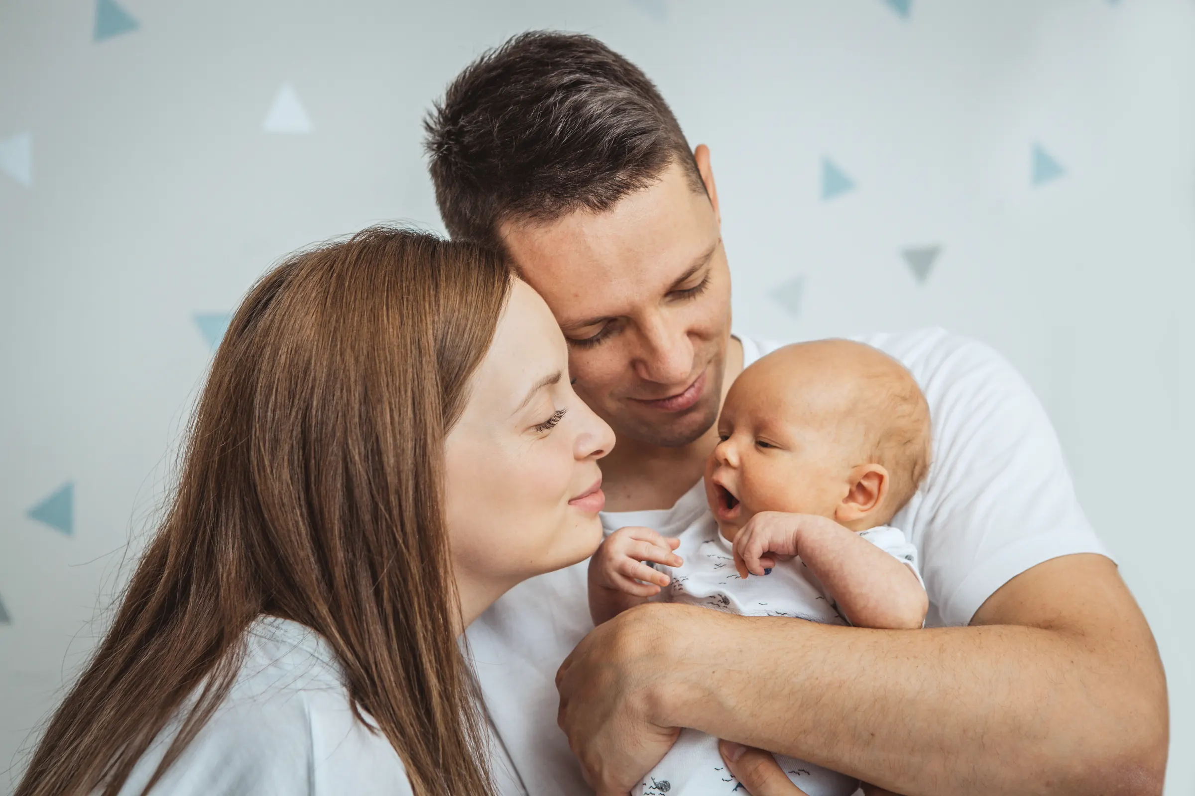 Junge Eltern halten ihr neugeborenes Baby im Arm und lächeln es an