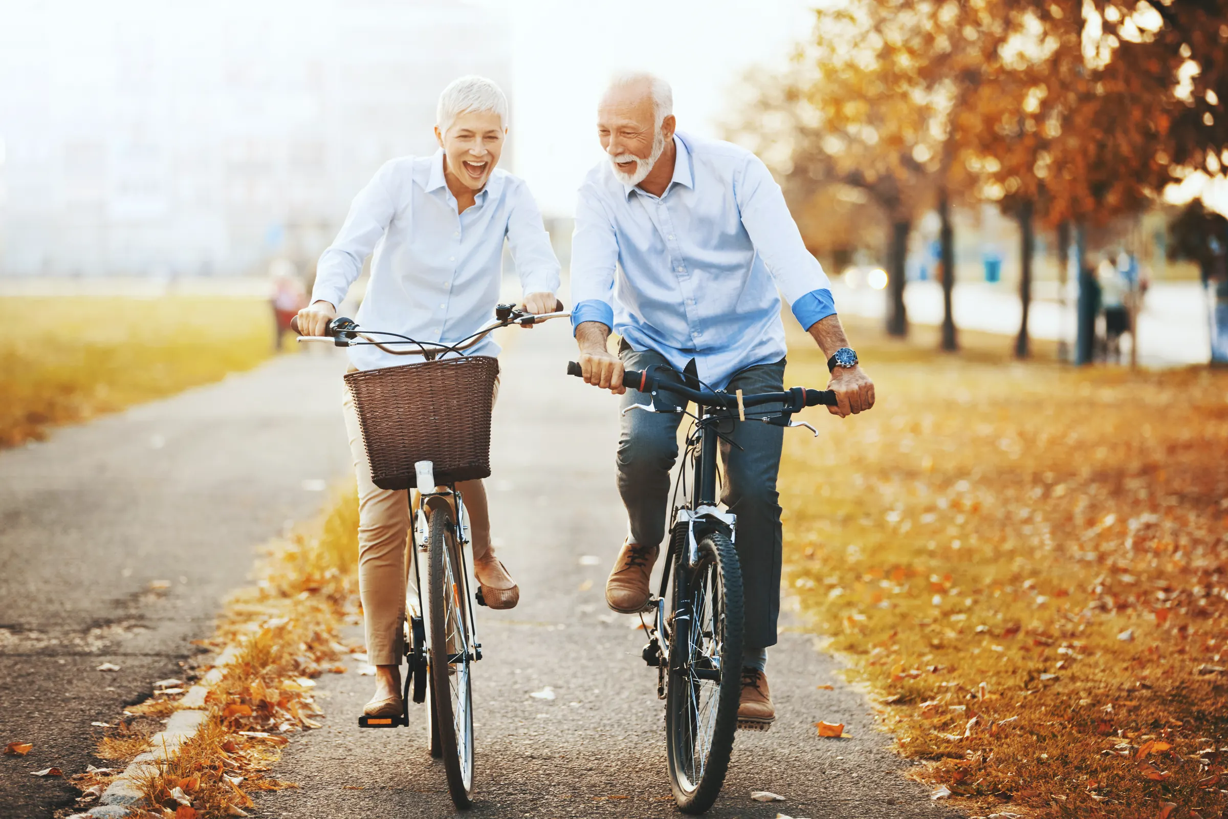 Älteres Paar fährt lachend Fahrrad durch eine herbstliche Allee