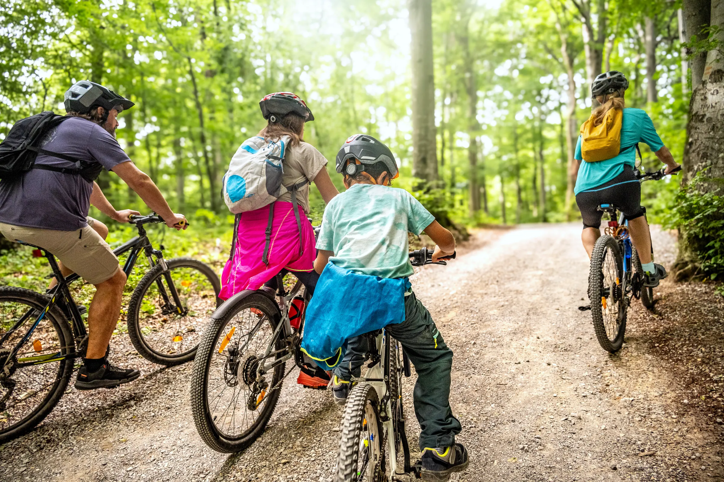 Familie mit zwei Kindern fährt mit Helmen auf einem sonnigen Waldweg Fahrrad