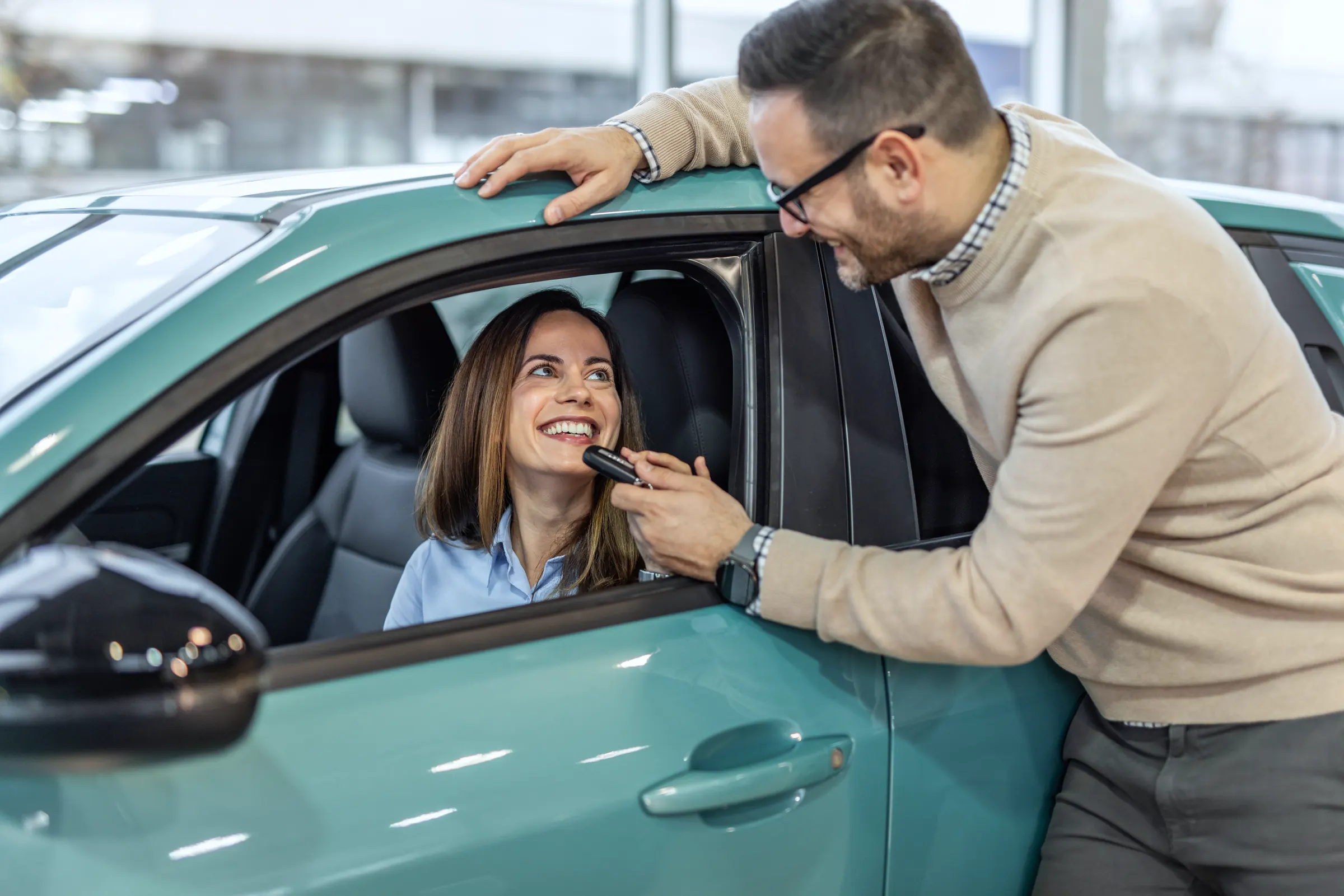 Mann übergibt seiner Partnerin am Fahrerfenster die Schlüssel für das neue Auto