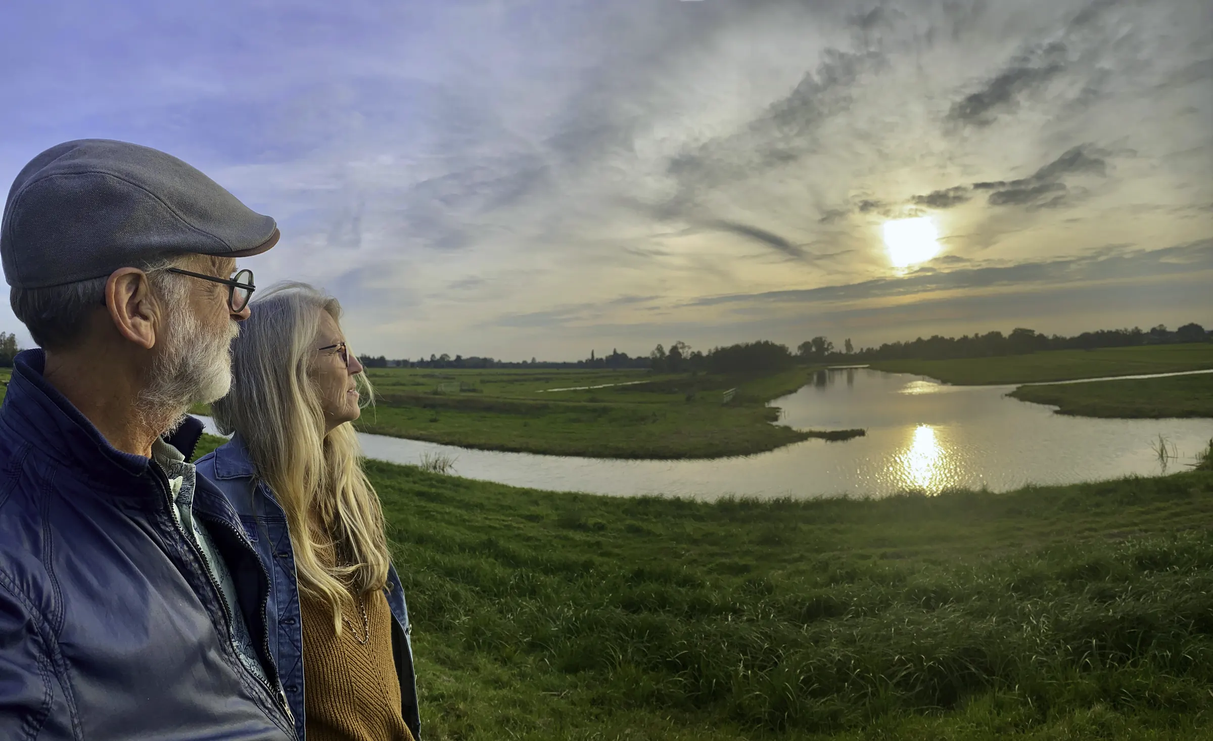 Älteres Paar blickt im Abendlicht über eine Flusslandschaft