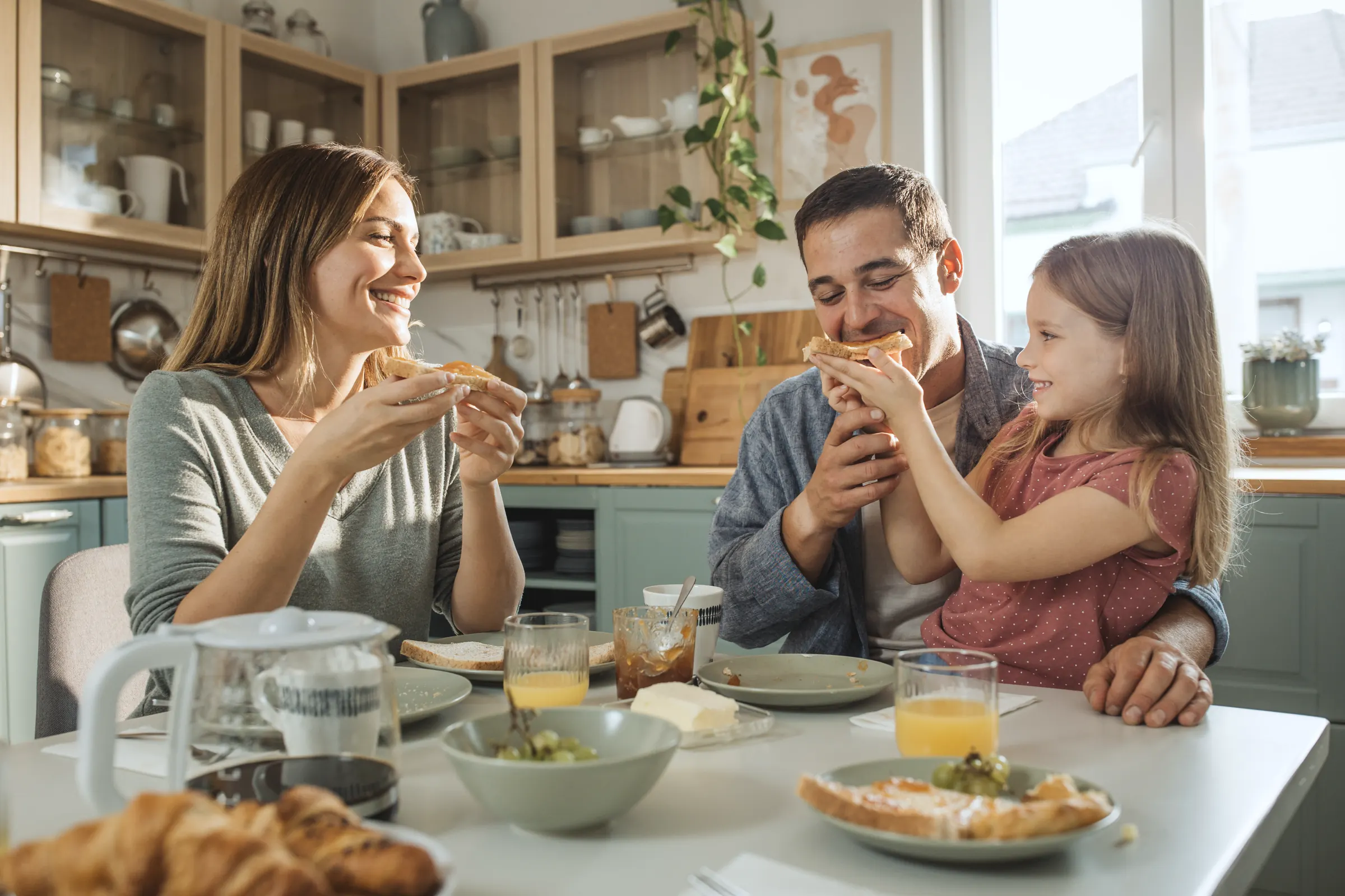 Eltern frühstücken mit ihrer kleinen Tochter am Küchentisch