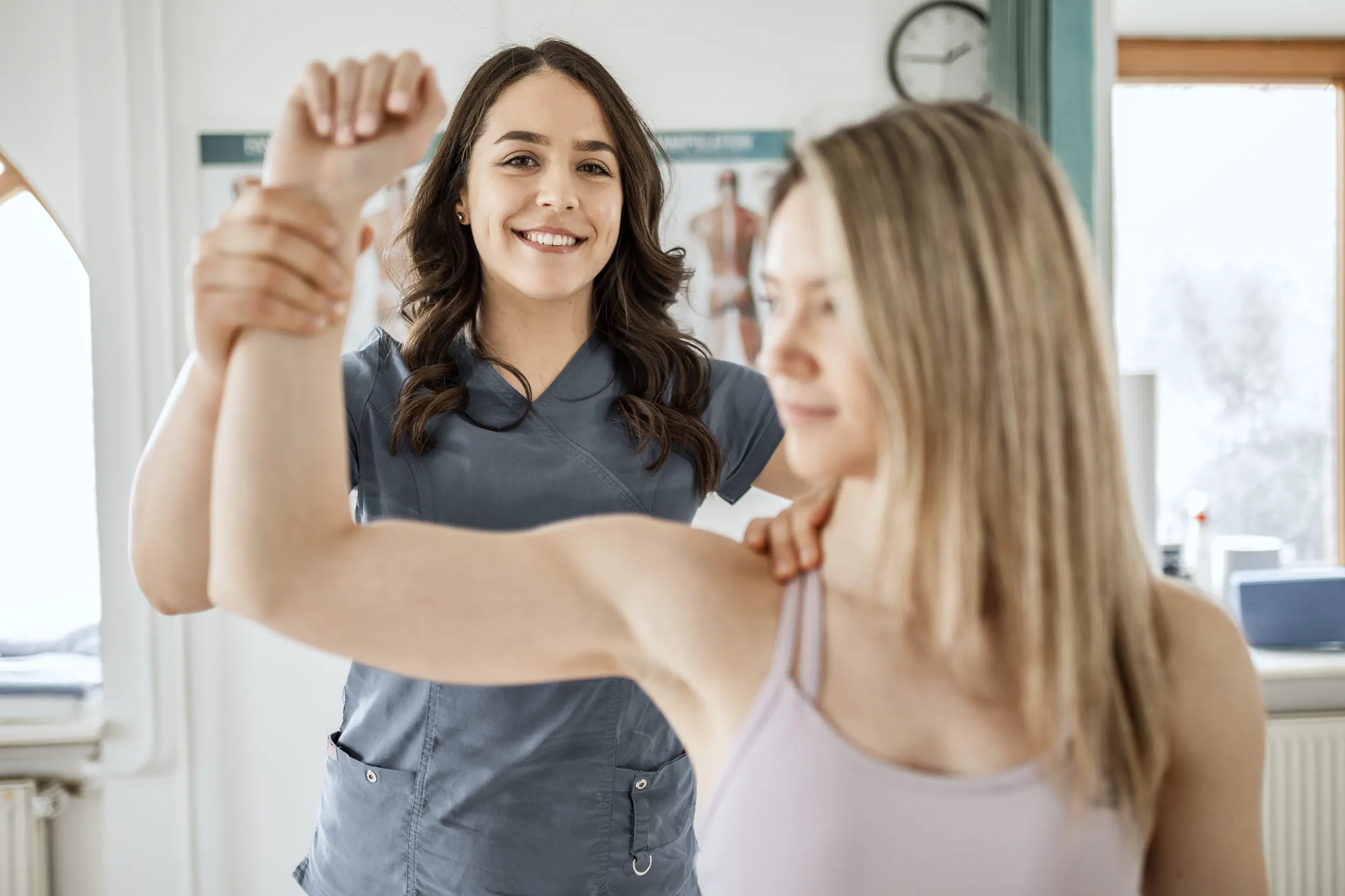 Physiotherapeutin bewegt in einer hellen Praxis den Arm einer Patientin