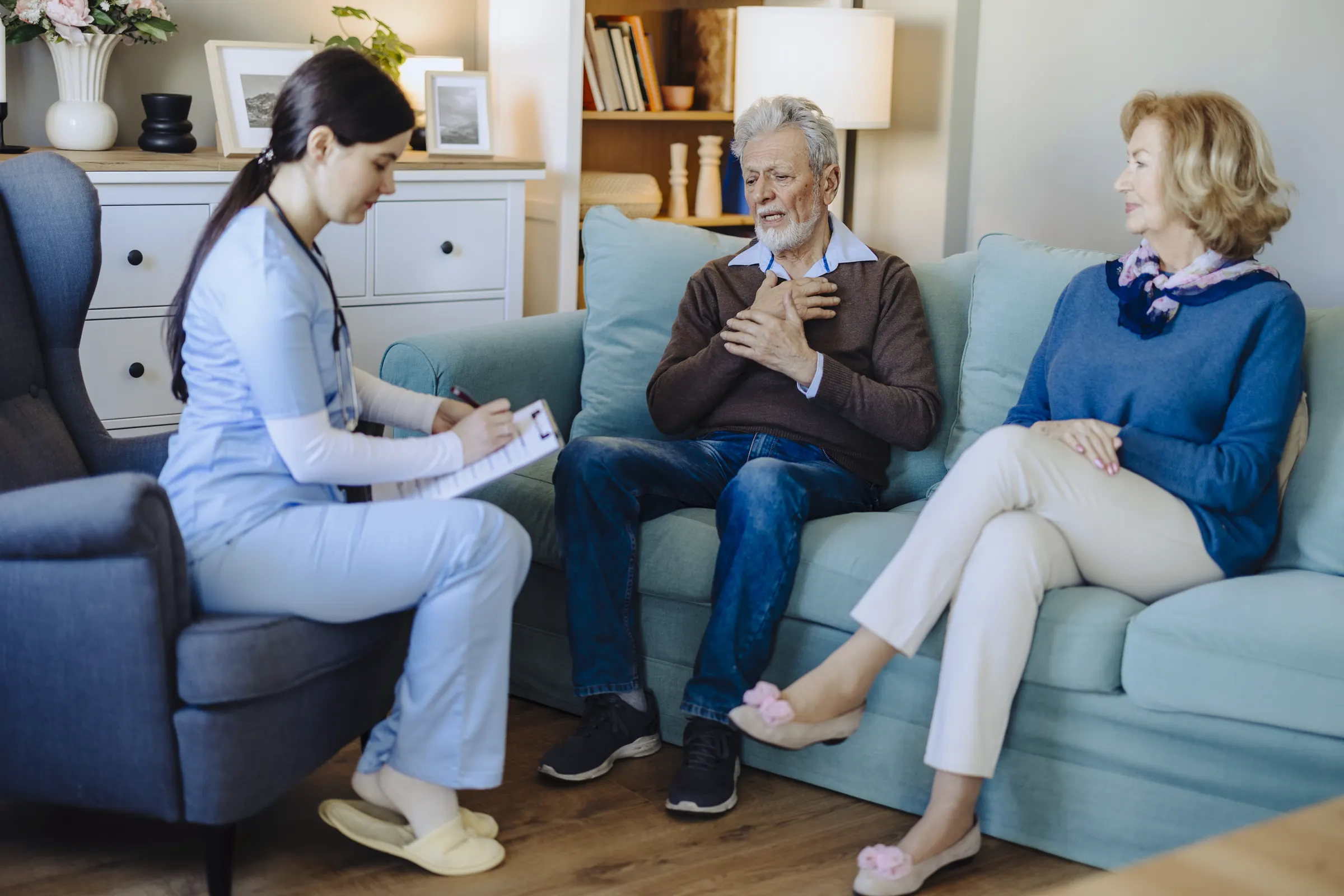 Pflegekraft im Gespräch mit einem älteren Paar im Wohnzimmer