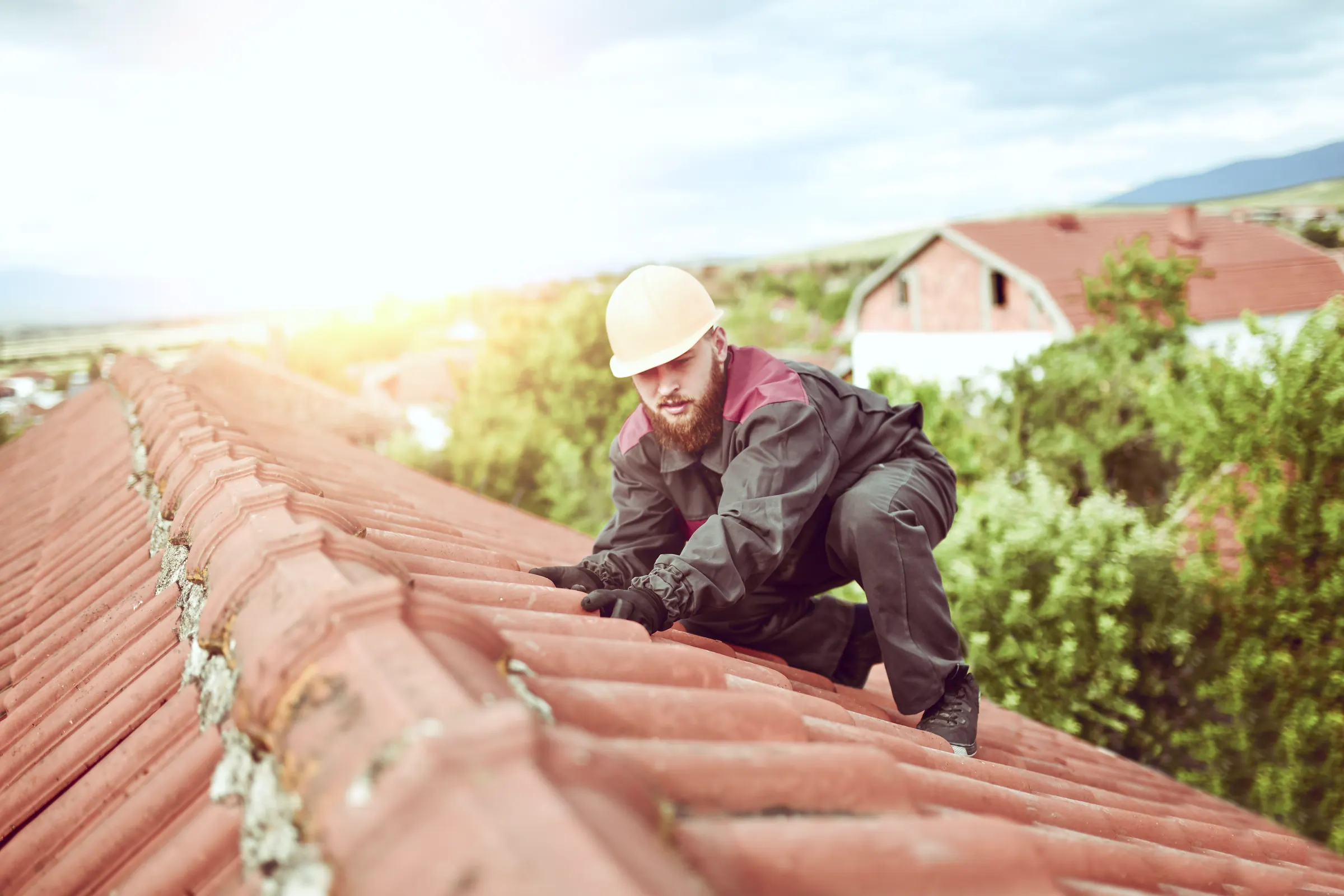 Dachdecker mit Helm arbeitet im Sonnenlicht auf einem roten Ziegeldach