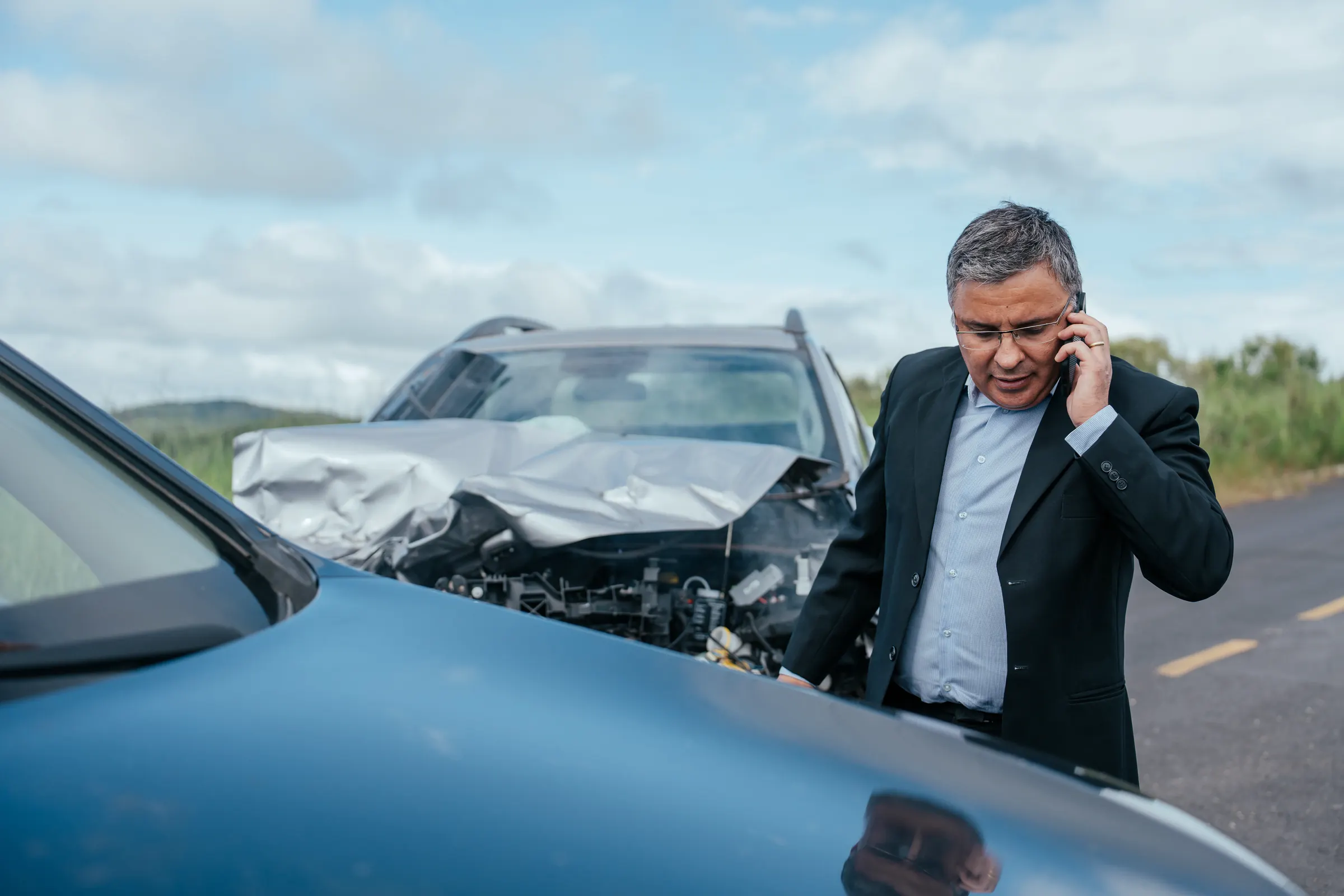 Mann im Sakko telefoniert nach einem Auffahrunfall neben den beschädigten Autos